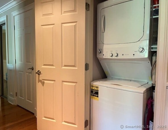 laundry area featuring stacked washer and clothes dryer, wood finished floors, and laundry area