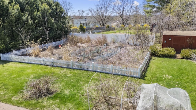 view of yard featuring fence, a storage unit, a garden, and an outbuilding