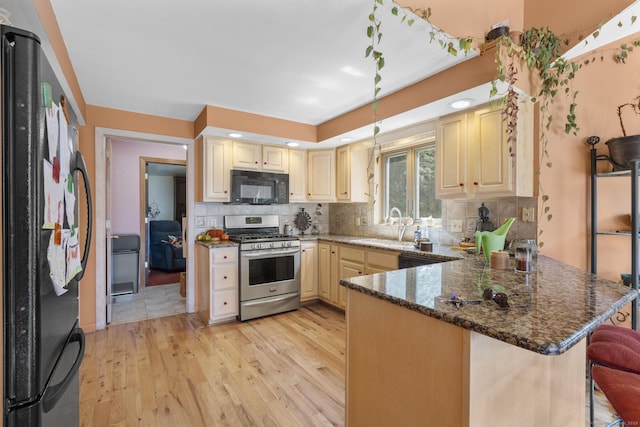kitchen featuring a sink, light wood-style floors, tasteful backsplash, black appliances, and a peninsula