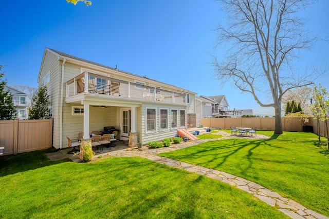 rear view of property with a balcony, a patio area, ceiling fan, a yard, and a fenced backyard