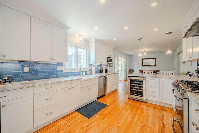 kitchen with a sink, stainless steel appliances, decorative backsplash, wine cooler, and white cabinetry