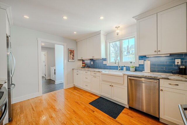 kitchen featuring light wood finished floors, a sink, backsplash, baseboards, and appliances with stainless steel finishes