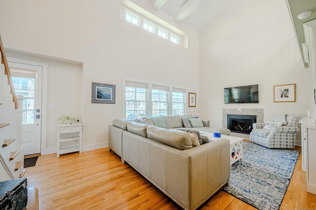 living area featuring stairway, light wood-type flooring, a high ceiling, and a fireplace