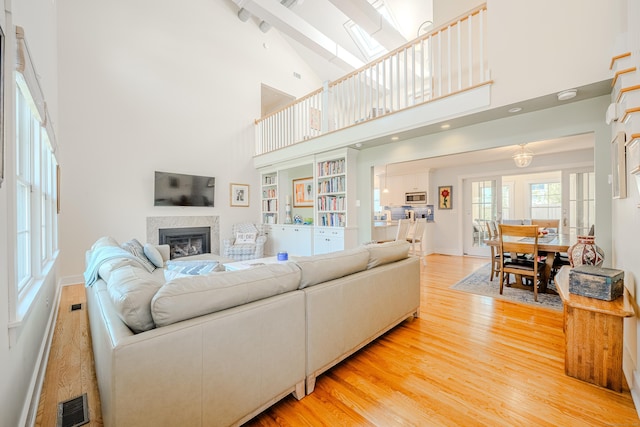 living room with a glass covered fireplace, visible vents, a towering ceiling, and light wood finished floors