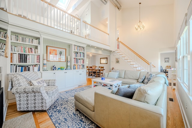 living room featuring wood finished floors, an inviting chandelier, stairs, visible vents, and a high ceiling