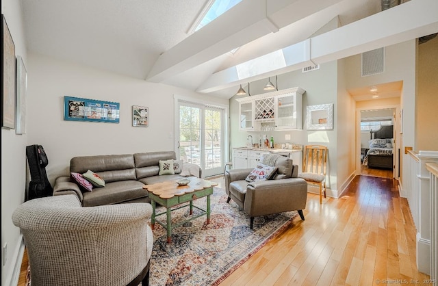 living area featuring visible vents, bar, light wood-style floors, and high vaulted ceiling