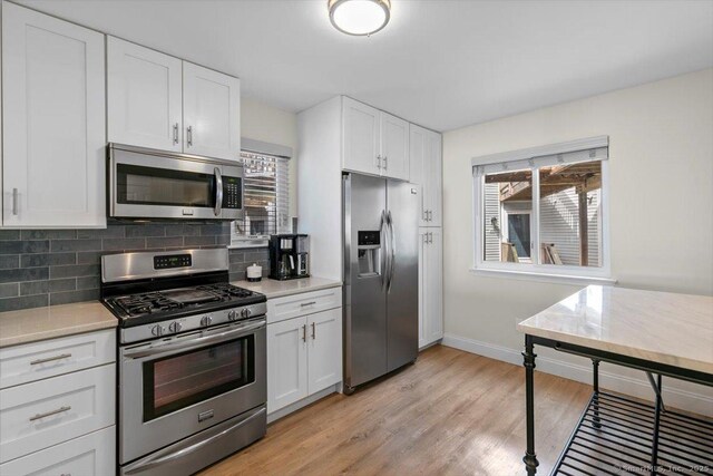 kitchen with decorative backsplash, light countertops, white cabinets, a wealth of natural light, and stainless steel appliances