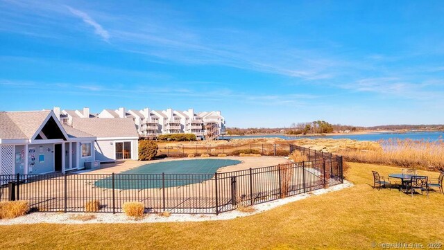pool with a water view, a patio area, fence, and a yard