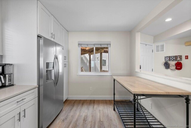 kitchen featuring light wood-style flooring, white cabinetry, baseboards, stainless steel refrigerator with ice dispenser, and visible vents