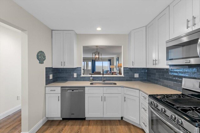 kitchen featuring light wood-style floors, white cabinets, a sink, backsplash, and stainless steel appliances