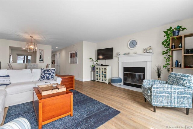 living area with baseboards, a fireplace with flush hearth, wood finished floors, and a chandelier