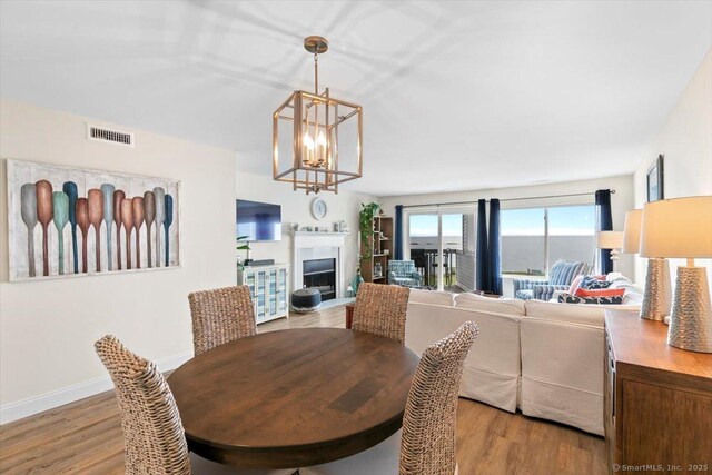 dining room featuring visible vents, a fireplace, wood finished floors, baseboards, and a notable chandelier