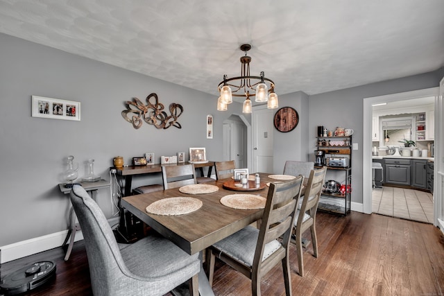 dining room with arched walkways, baseboards, and dark wood finished floors