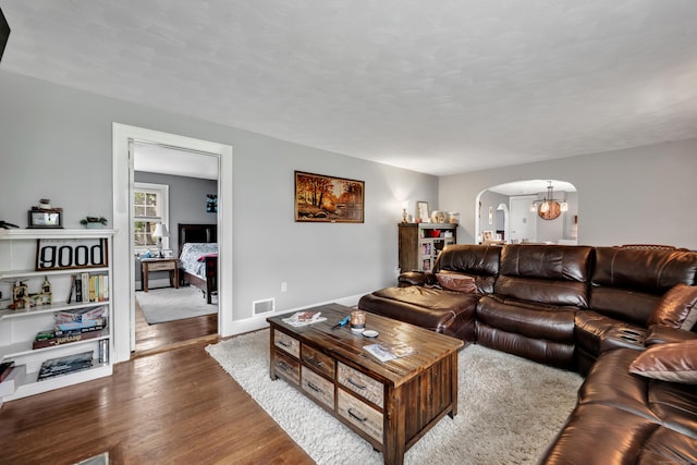 living room with dark wood-type flooring, visible vents, an inviting chandelier, arched walkways, and baseboards
