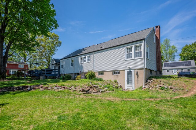 rear view of property featuring a chimney, a lawn, and a deck