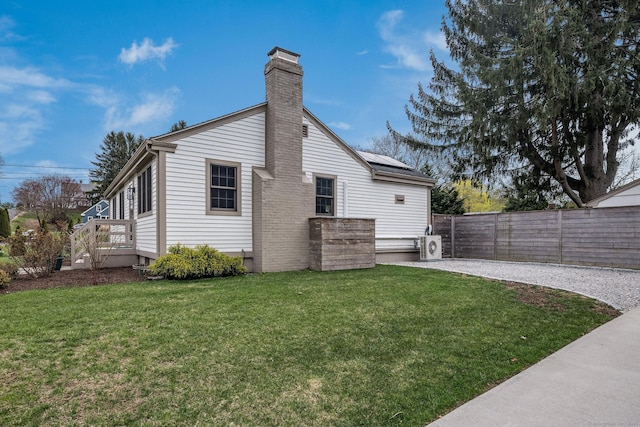 back of property with fence, a chimney, a yard, and solar panels