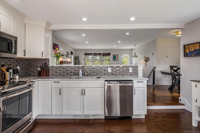 kitchen with appliances with stainless steel finishes, tasteful backsplash, light stone counters, white cabinets, and a peninsula