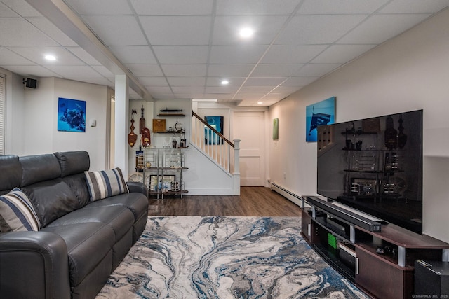 living room with wood finished floors, a drop ceiling, baseboard heating, stairway, and recessed lighting