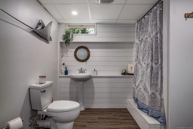 full bath with a paneled ceiling, wood finished floors, toilet, shower / tub combo with curtain, and wooden walls