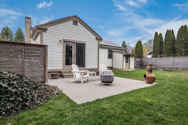rear view of property with a yard, a chimney, roof mounted solar panels, and a patio area