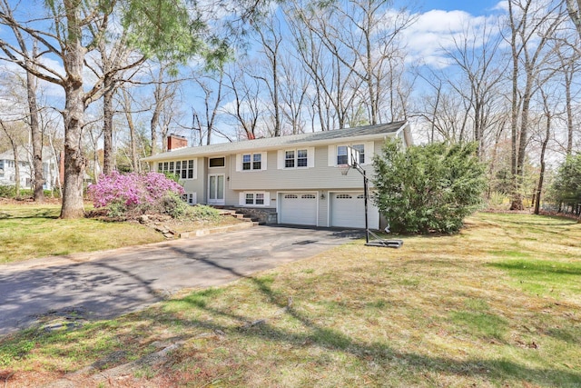 bi-level home with an attached garage, driveway, a chimney, and a front yard