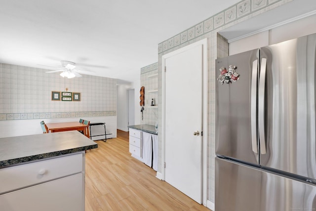 kitchen with dark countertops, freestanding refrigerator, a ceiling fan, wallpapered walls, and a baseboard heating unit