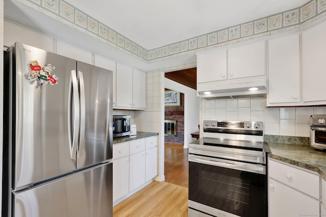 kitchen with white cabinets, appliances with stainless steel finishes, backsplash, light wood-type flooring, and under cabinet range hood