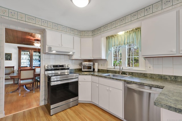 kitchen with a sink, under cabinet range hood, light wood-style floors, stainless steel appliances, and white cabinetry