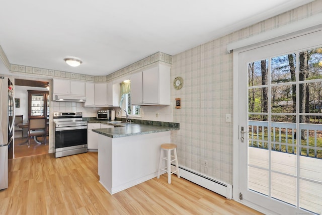 kitchen featuring a peninsula, wallpapered walls, under cabinet range hood, a baseboard heating unit, and stainless steel appliances