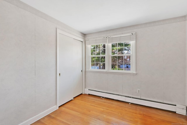 unfurnished bedroom with a closet, a baseboard heating unit, and light wood finished floors