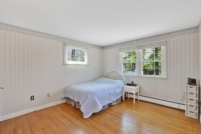 bedroom featuring light wood finished floors, a baseboard heating unit, multiple windows, and wallpapered walls