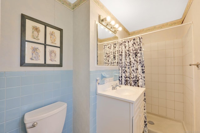 full bathroom with a tile shower, vanity, toilet, a wainscoted wall, and tile walls