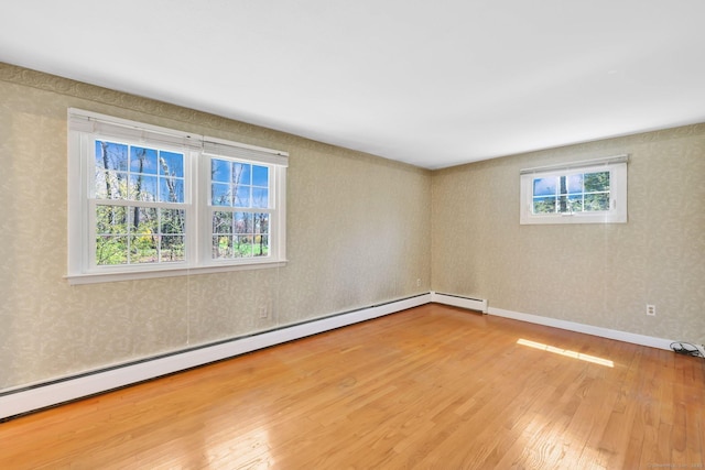 empty room featuring baseboards, a baseboard heating unit, wallpapered walls, and wood finished floors