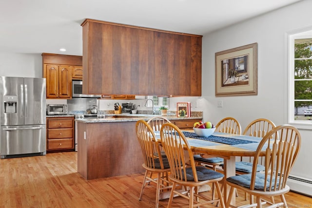 kitchen with brown cabinetry, a peninsula, recessed lighting, light wood finished floors, and appliances with stainless steel finishes
