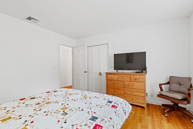 bedroom with visible vents, light wood-style flooring, and a closet