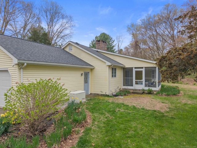 view of front of home featuring a shingled roof, a sunroom, a front lawn, and a chimney