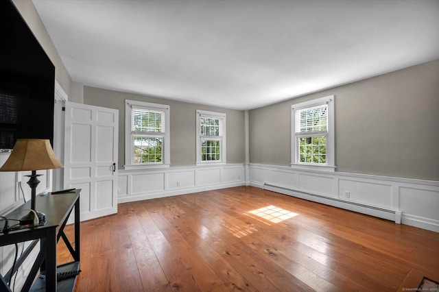 interior space with a healthy amount of sunlight, baseboard heating, wainscoting, and hardwood / wood-style flooring