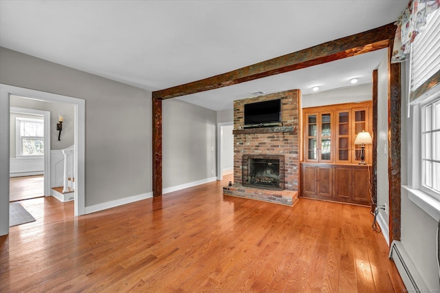 unfurnished living room featuring baseboard heating, a brick fireplace, beamed ceiling, a baseboard heating unit, and light wood-style flooring