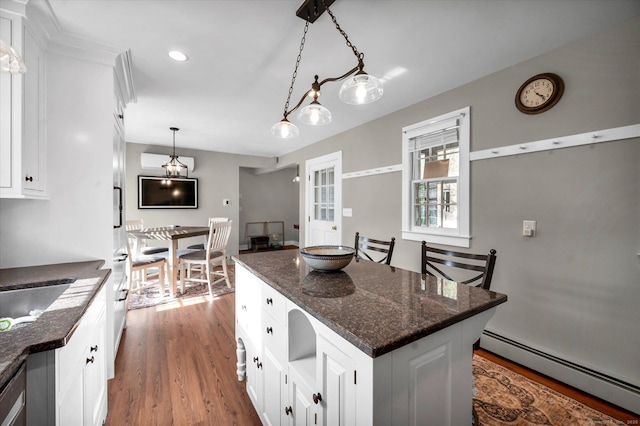 kitchen with white cabinets, hanging light fixtures, baseboard heating, wood finished floors, and a kitchen island