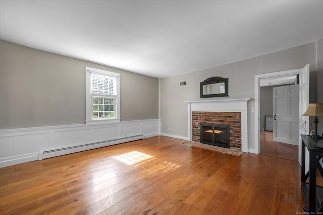 unfurnished living room featuring a fireplace, a baseboard heating unit, hardwood / wood-style flooring, and visible vents