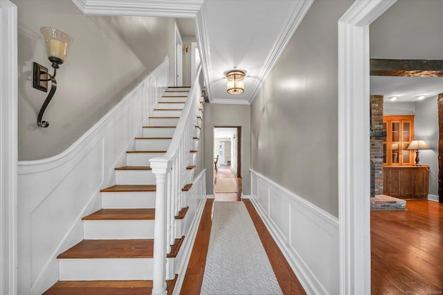 stairway featuring crown molding, a decorative wall, wood finished floors, and a wainscoted wall