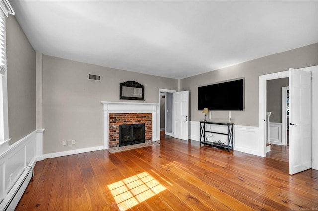unfurnished living room with a wainscoted wall, baseboard heating, hardwood / wood-style floors, and visible vents