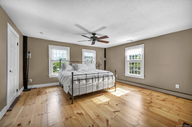 bedroom with ceiling fan, a textured ceiling, light wood-style flooring, baseboards, and a baseboard heating unit