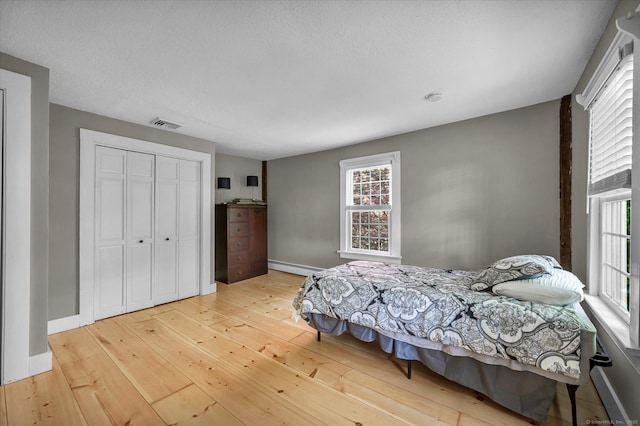 bedroom featuring a closet, multiple windows, baseboard heating, and hardwood / wood-style flooring