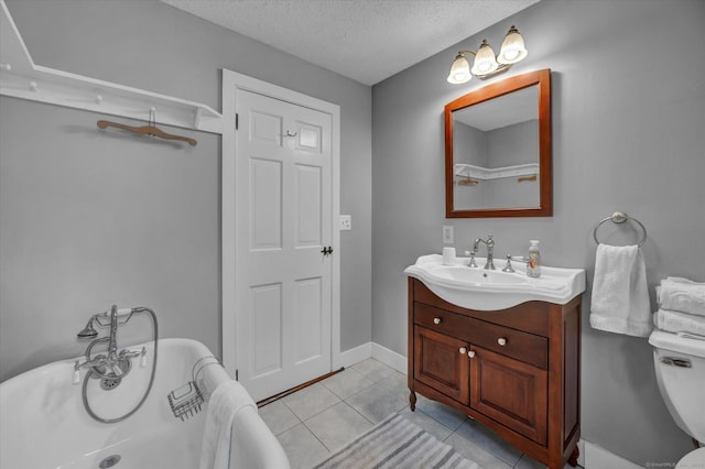 full bathroom featuring tile patterned flooring, vanity, toilet, a textured ceiling, and a freestanding tub