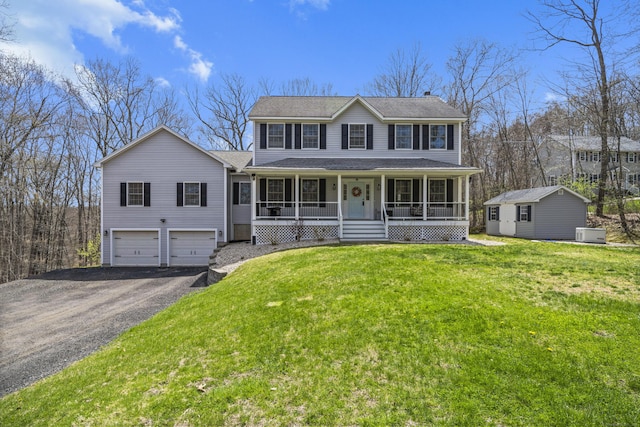 colonial house featuring an outdoor structure, covered porch, aphalt driveway, a front lawn, and an attached garage