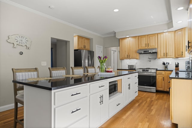 kitchen with appliances with stainless steel finishes, a breakfast bar, a kitchen island, light wood finished floors, and ornamental molding