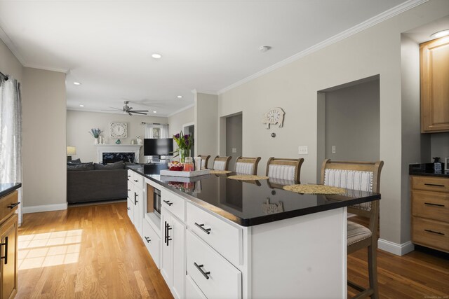 kitchen with light wood-style flooring, ornamental molding, dark countertops, ceiling fan, and a kitchen breakfast bar