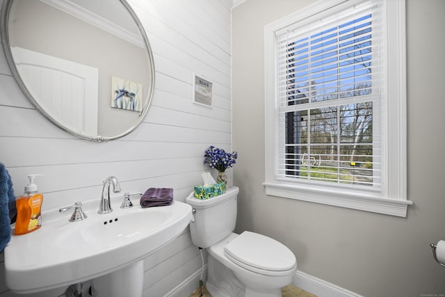 half bathroom with wood walls, toilet, baseboards, and a sink