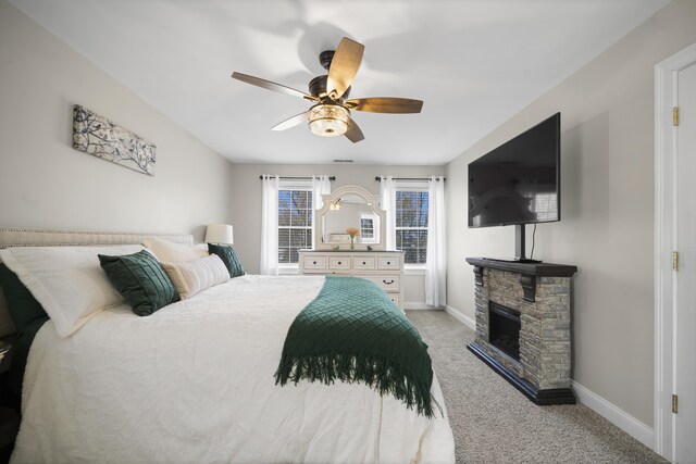 carpeted bedroom with baseboards, ceiling fan, and a stone fireplace